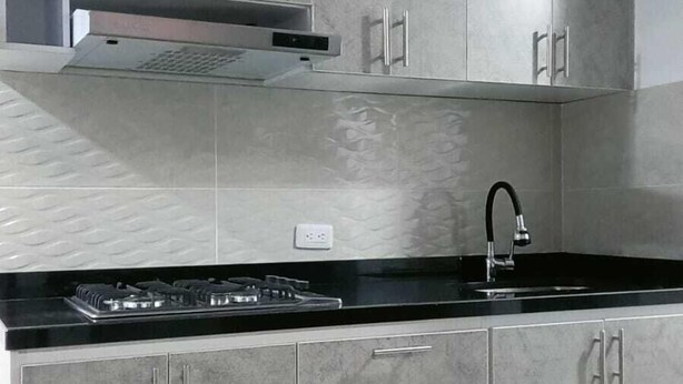 A kitchen with grey cabinets, a black countertop, and a stainless steel range hood. - Aparta Hotel Los Nogales (Bogotá)