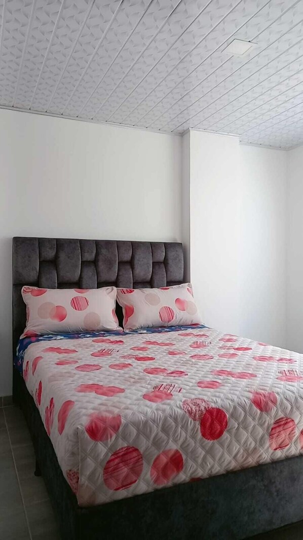 A bedroom with a bed, a headboard, and a patterned ceiling.