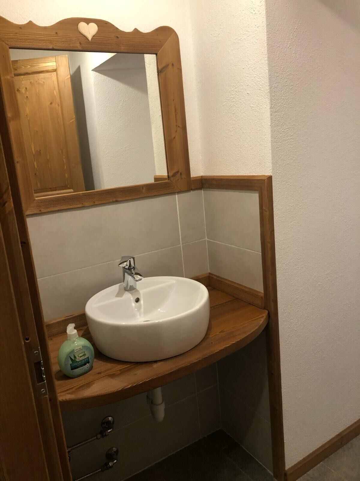 Een badkamer met een houten wastafelmeubel, een witte wasbak en een spiegel met een hartvormig detail.