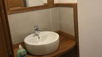 Een badkamer met een houten wastafelmeubel, een witte wasbak en een spiegel met een hartvormig detail.