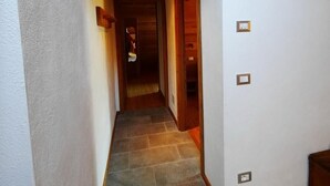 Un couloir étroit avec des poutres en bois au plafond, un sol carrelé et une porte donnant sur une autre pièce.