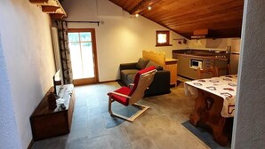Un intérieur chaleureux avec un plafond en bois, un coin repas et un espace salon agrémenté d’un fauteuil rouge.