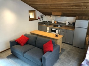 Une cuisine compacte avec une table en bois, un canapé gris agrémenté de coussins rouges et une petite fenêtre.