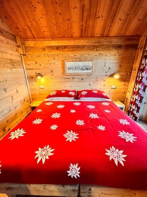 Une pièce de style cabane en bois, avec un lit, deux lampes fixées au mur et un tableau encadré accroché au mur.