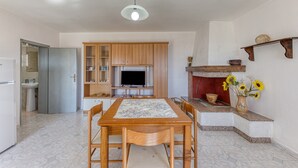 A kitchen with a dining table, chairs, a TV, cabinets, a refrigerator, and a fireplace with a vase of sunflowers. - Apartment 'Villino Scapucci' with Sea View, Private Terrace and Air Conditioning (Santa Maria di Leuca)