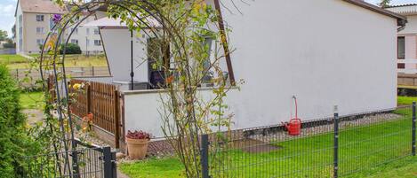 Ein weißes Gebäude mit einem Metallgitter und einem kleinen Garten mit einer blühenden Pflanze.