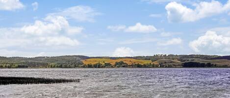Een meer met kalm water en een vergezichte van glooiende heuvels onder een heldere lucht.