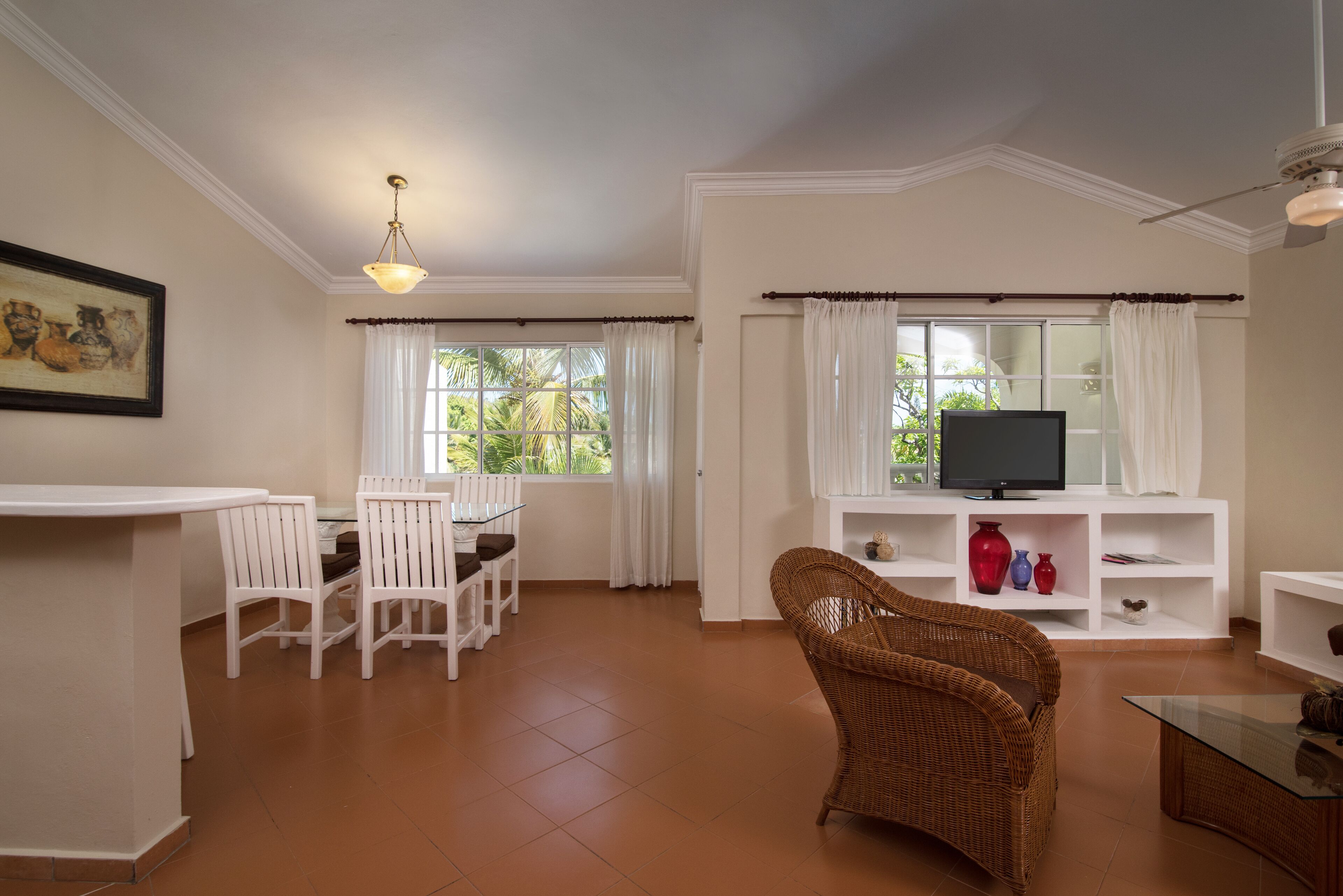 A living room with a television, white furniture, and a wicker chair.