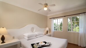Ein ordentlich eingerichtetes Hotelzimmer mit einem großen Bett, zwei Nachttischen mit Lampen, einem Deckenventilator und einem Fenster mit Vorhängen.