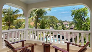 Ein Balkon mit Holzstühlen und einem kleinen Tisch mit Blick auf einen Pool und Palmen.