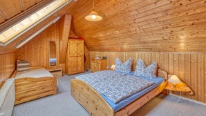 A wooden room with a sloped ceiling, a bed with patterned bedding, a nightstand, a dresser, and a mirror.