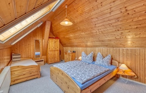 A wooden room with a sloped ceiling, a bed with patterned bedding, a nightstand, a dresser, and a mirror.