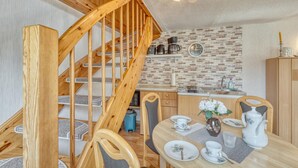 A wooden staircase leading to a loft bedroom, a kitchen with brick backsplash, and a dining area with a table set for two.