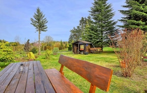 A wooden bench and picnic table in a park with a small cabin and a bench nearby.