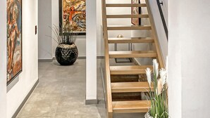 Un interior moderno con una escalera de madera, una planta en maceta y obras de arte en las paredes.
