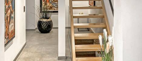 Un interior moderno con una escalera de madera, una planta en maceta y obras de arte en las paredes.