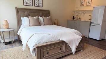 Un dormitorio con una cama grande, una mesita de noche pequeña, una alacena y una kitchenette, además de un refrigerador.