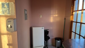 Una pequeña cocina equipada con refrigerador, un basurero y una ventana.