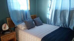 Un dormitorio con cama, mesita de noche y ventana con cortinas.