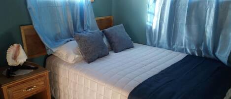 A bedroom with a bed, a nightstand, and a window with curtains.