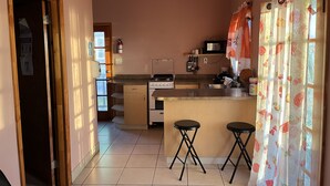 Una cocina con estufa, lavamanos y taburetes de bar. Hay un extintor en la pared y un microondas sobre la estufa.