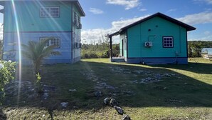 Una casa de dos pisos con fachada verde y un balcón, rodeada por un jardín con césped y un pequeño estanque.