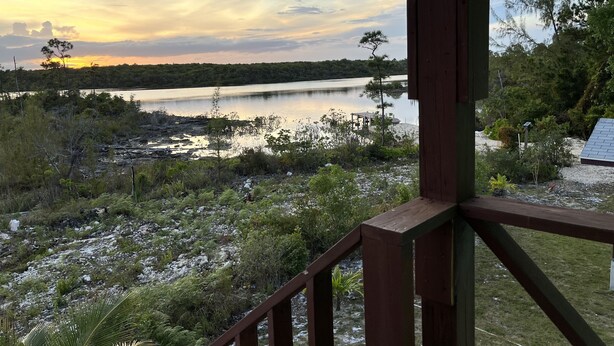 Vista al lago desde una terraza de madera con barandilla, rodeada de vegetación y una orilla distante.