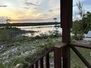 A lakeside view from a wooden deck with a railing, surrounded by vegetation and a distant shoreline.