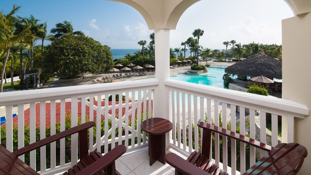 A balcony with a pool view, white railings, and outdoor seating.