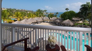 A balcony with a pool, thatched umbrellas, and a view of the ocean and palm trees.