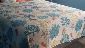 Makuuhuoneessa on sänky, yöpöytä, seinäkello ja ikkuna, jossa on sälekaihtimet.