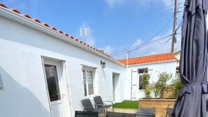Une terrasse extérieure avec une table et des chaises, un parasol et une vue sur un bâtiment blanc avec un toit rouge.