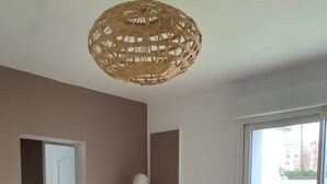 Une pièce avec une table basse blanche, un luminaire suspendu en osier et une vue sur l’extérieur, accessible par une porte-fenêtre coulissante.