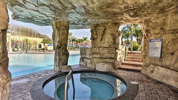 A spa area with a hot tub, stone pillars, and a pool.