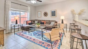 A living room with a sofa, coffee table, and chairs, a patterned rug, and a ceiling fan.