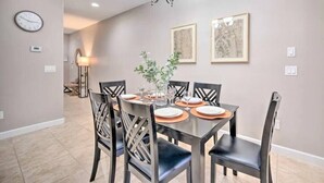 A dining area with a table set for four, surrounded by chairs, a chandelier, and framed artwork on the wall.