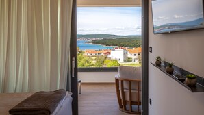 Un balcón con vistas a un pueblo costero, una cama, una silla y una estantería con plantas.