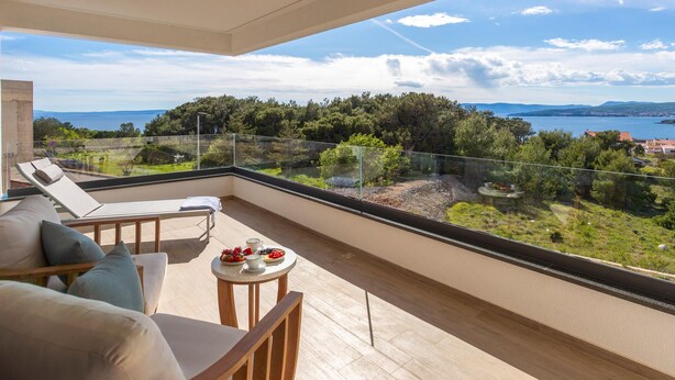 Un balcón con vista al mar y a los árboles, una mesa con fruta y un sofá con cojines.