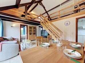 Un coin repas avec une table en bois dressée pour quatre personnes, un escalier et une cuisine visible au fond.