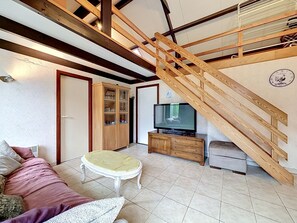Un salon comprenant un canapé, une petite table, un téléviseur, un meuble et un escalier en bois.