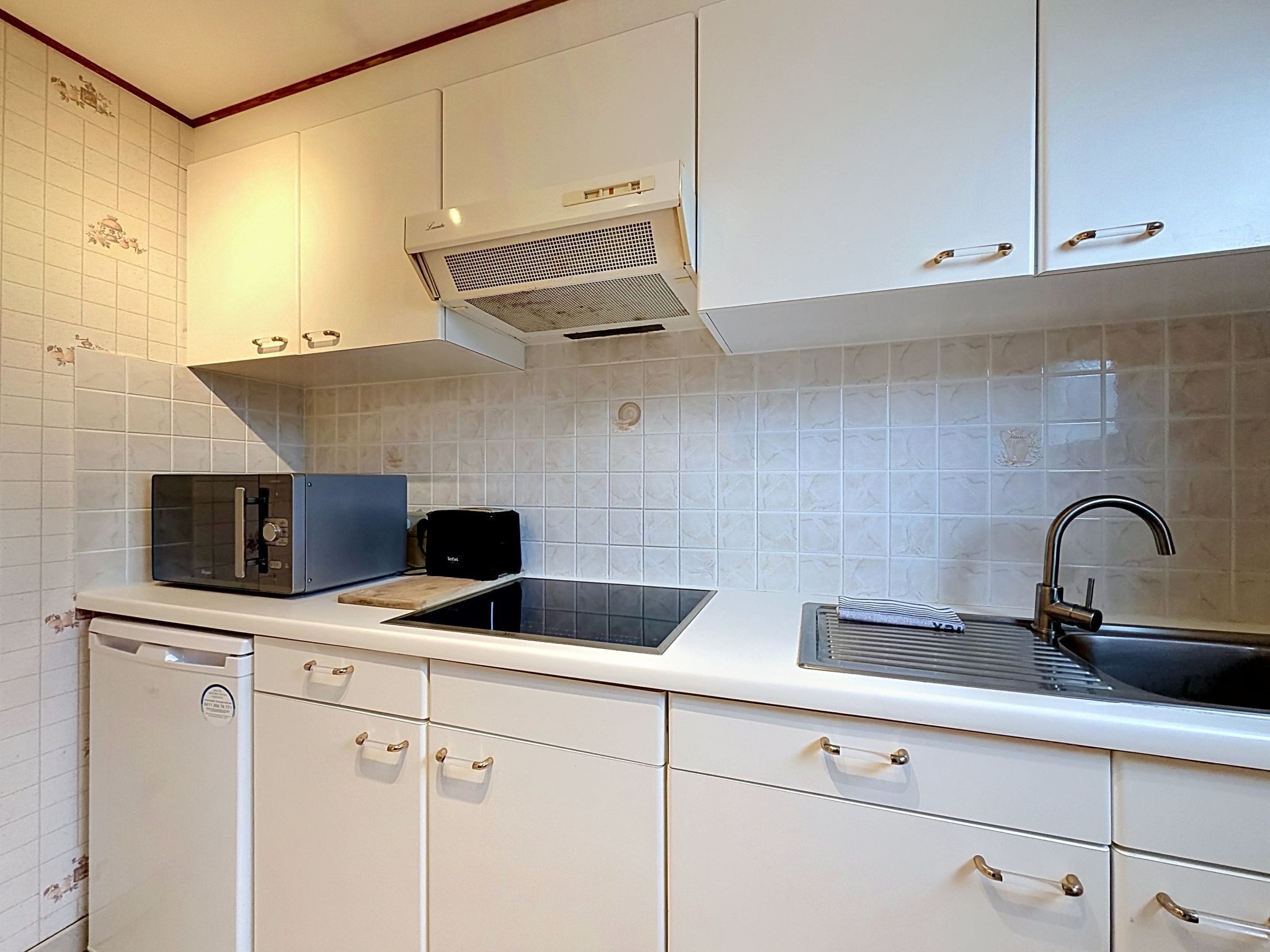Una cocina moderna con armarios blancos, microondas integrado, tostadora y un lavabo con grifo.