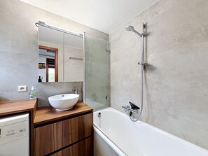 Une salle de bain moderne avec une baignoire blanche, un meuble-lavabo en bois avec un vasque blanche et une douche séparée par une paroi de verre.
