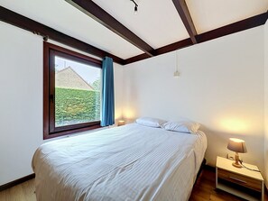 Une chambre à coucher avec un grand lit, une table de chevet, une lampe et une fenêtre avec des rideaux.