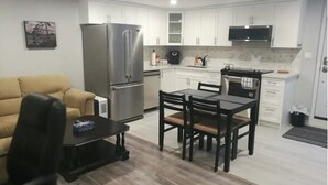 A modern kitchen with white cabinets, a stainless steel refrigerator, and a dining area with a table and chairs. - Beautiful 2-bedroom Guest Home in Guelph (Guelph)