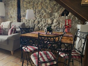 Un comedor acogedor con pared de piedra, una mesa de madera, sillas de metal y una lámpara.