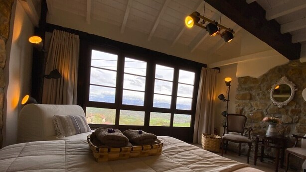 Une chambre spacieuse avec un grand lit, un mur en pierre et une vue sur la campagne, visible à travers de grandes fenêtres.