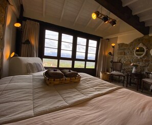 Un dormitorio amplio con una cama grande, una pared de piedra y vistas al campo a través de amplias ventanas.