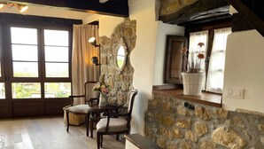 Une pièce chaleureuse avec un mur en pierre, des poutres en bois au plafond, une table à manger avec des chaises et une grande fenêtre avec des rideaux.