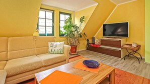 A living room with a sofa, a television, a wooden coffee table, and a potted plant. - Ferienwohnung Waren (Müritz) (Waren (Müritz))