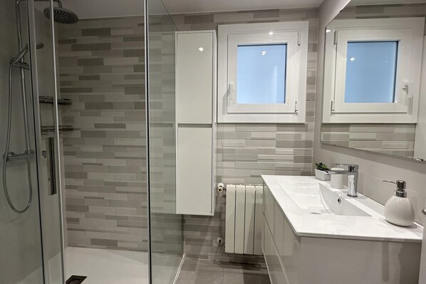 A modern bathroom with a glass shower enclosure, a white sink with a mirror above, and a tiled backsplash.